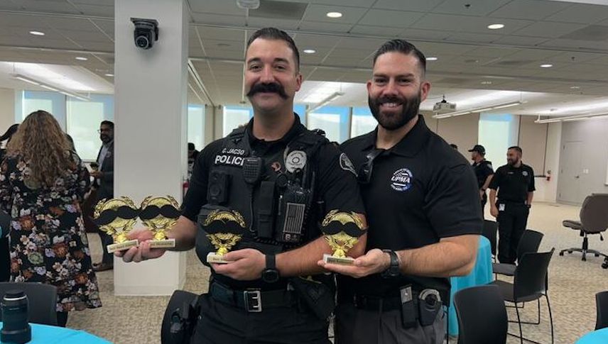 Two officers stand side by side holder trophies, smiling