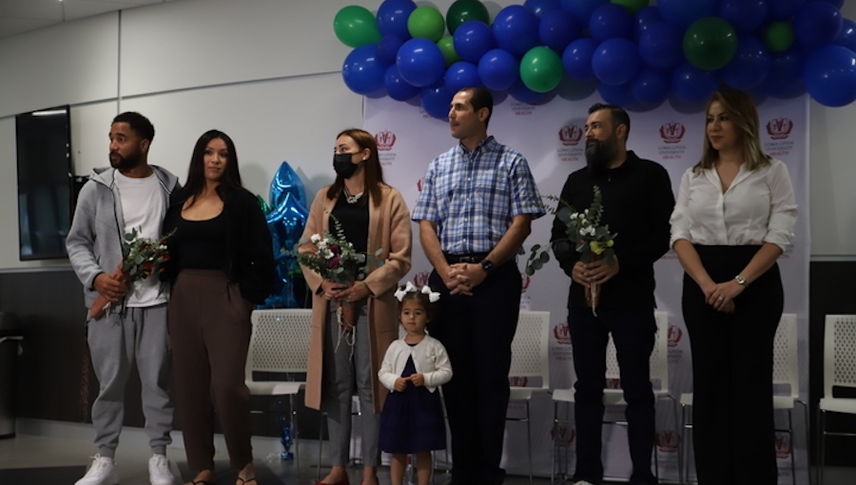 Six people stand shoulder to shoulder in front of blue and green balloon backdrop.
