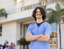 Nito Gil standing with arms crossed wearing blue LLUH scrubs