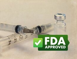 clear vaccine vial next to needle with green badge that says "FDA APPROVAL"