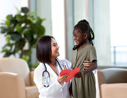 Picture of doctor hugging child while holding a cut-out of a heart 