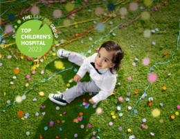 young boy with brown hair sitting in the grass, looking up with confetti falling.
