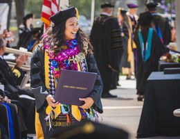 Female graduate in cap and gown wearing floral lei after accepting degree.