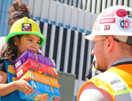 young girl scout holds colorful cookie boxes in front of kneeling construction worker