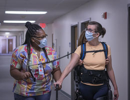 Woman walking down the hall with rehabilitation equipment being helped by another woman