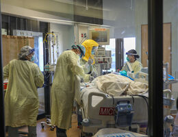 healthcare workers wearing masks and gowns caring for COVID-19 patient