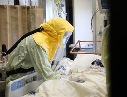 Physician wearing personal protective equipment leans over a COVID-19 patient's bedside in the Loma Linda University Medical Intensive Care Unit.