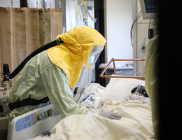 Physician wearing personal protective equipment leans over a COVID-19 patient's bedside in the Loma Linda University Medical Intensive Care Unit.