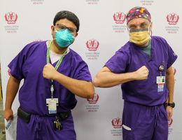 Two attending physicians stand flexing their arms in front of LLUH backdrop