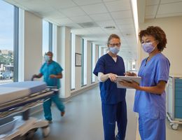 caucasion female nurse in navu scrubs and Black nurse in light blue scrubs in a hospital hallway, looking at a piece of paper