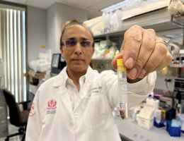 Middle eastern man holding test tube in front of him with cancer cells inside.