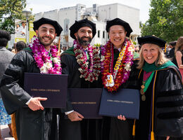 Four college graduates in their cap and gowns, holding their degrees
