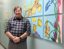 Dr. Daniel Lamb stands in hallway in front a painting of turtles and fish
