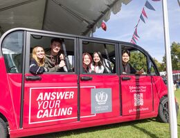 College students in a red, over-sized golf cart, smiling at the camera