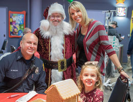 fireman, santa, mom, and kid pose for picture next to gingerbread house