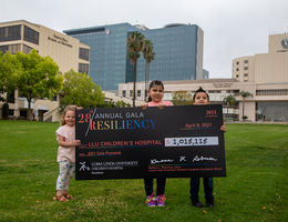 three kids standing in front of hospital with giant check