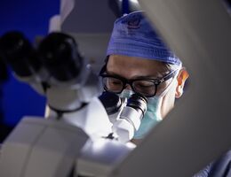 Male doctor in glasses looks through microscope in preparation for brain tumor surgery