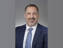 Caucasian male in a navy business suit, with a goatee and mustache