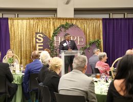 Jeevaka Weerasinghe addresses the audience seated at tables in a large room