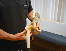 Doctor in black scrubs holding a model of a hip bone