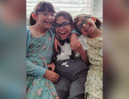 Aiden sitting and smiling with his sisters