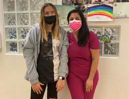 tall female patient poses for photo, hugging smiling female doctor in scrubs