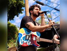 Brandon singing at a microphone with a multicolored guitar strapped over his shoulder