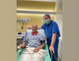 Caucasian man in a hospital bed with his doctor standing beside him in blue scrubs