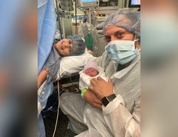 first-time parents smile for photo after a c-section procedure, dad holds baby boy in his arms