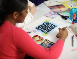 Girl in a red shirt writes on a vision board at a table with crafting supplies