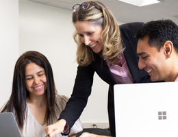 Female Caucasian teacher with male and female college student looking at computers.