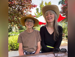 Two Caucasion women sitting outside, smiling, wearing sun hats