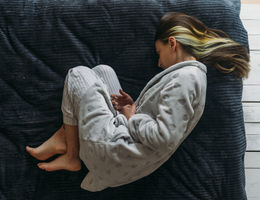 Caucasian woman laying on her side holding her stomach. Photo taken from above