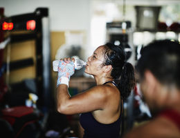 Sweating female boxer drinking water after workout in boxing gym - stock photo