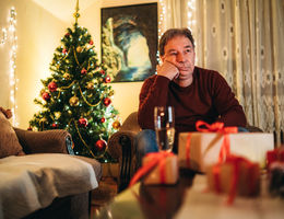 Senior caucasian man sitting on a couch and waiting alone for Christmas / New Year's eve.