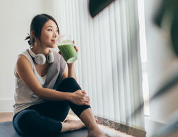 Woman taking a break from exercise to drink a green smoothie