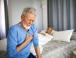 Senior man sitting on edge of bed holding chest in pain