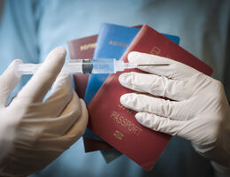 An unidentifiable person holding a syringe over a pile of passports.
