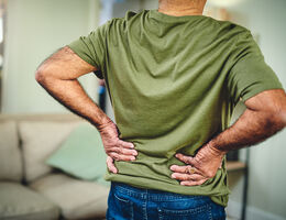 Cropped shot of a senior man in a green shirt holding his lower back suffering from back pain