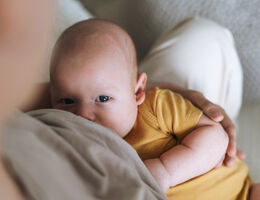 Young mother breastfeeding your 2-3 month baby boy lying on blanket at home