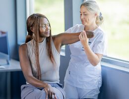 A black woman amputee and a white nurse stretch her arm