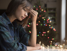 The post-holidays blues are a real thing that can last up to two weeks Women with her head on her hand in sadness with a Christmas tree in the background