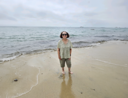 A female stands in the sand on the beach on an overcast day with the ocean water behind her