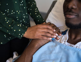 Woman holding man's hand as he lies in a hospital bed