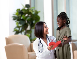 Female physician with young Black female holding a red paper heart