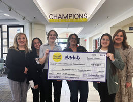 six women smiling at the camera holding a large check