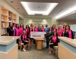 Group of people wearing pink in honor of breast cancer awareness month, during a check presentation with a large check for $200,000