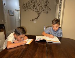 Two young boys sitting at a table working on work books