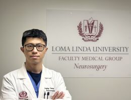 Doctor with a white coat stands in front of the Loma Linda University Neurosurgery sign with his arms crossed