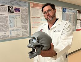 Jared Inman, MD, a head and neck surgical oncologist at Loma Linda University Health, holds a 3D replica of a human skull, around which various cancers can form.